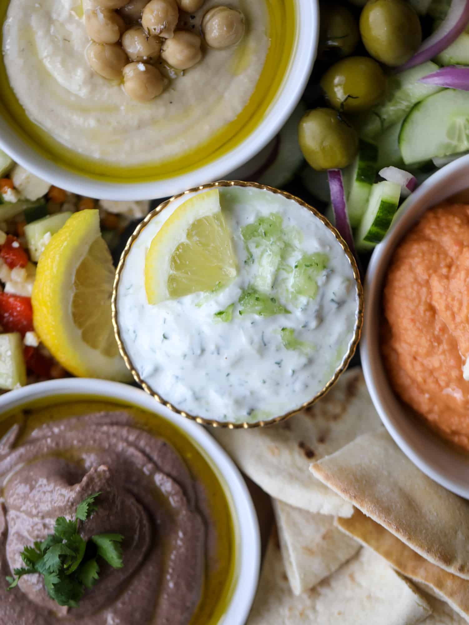 Here you can find out how to make the perfect hummus platter! This trio includes caramelized onion hummus, smoky black bean hummus and roasted red pepper white bean hummus, along with a couscous salad and quick tzatziki! I howsweeteats.com #hummus #platter #appetizer #snack #chickpeas #healthy #blackbeans #yogurt #tzatziki