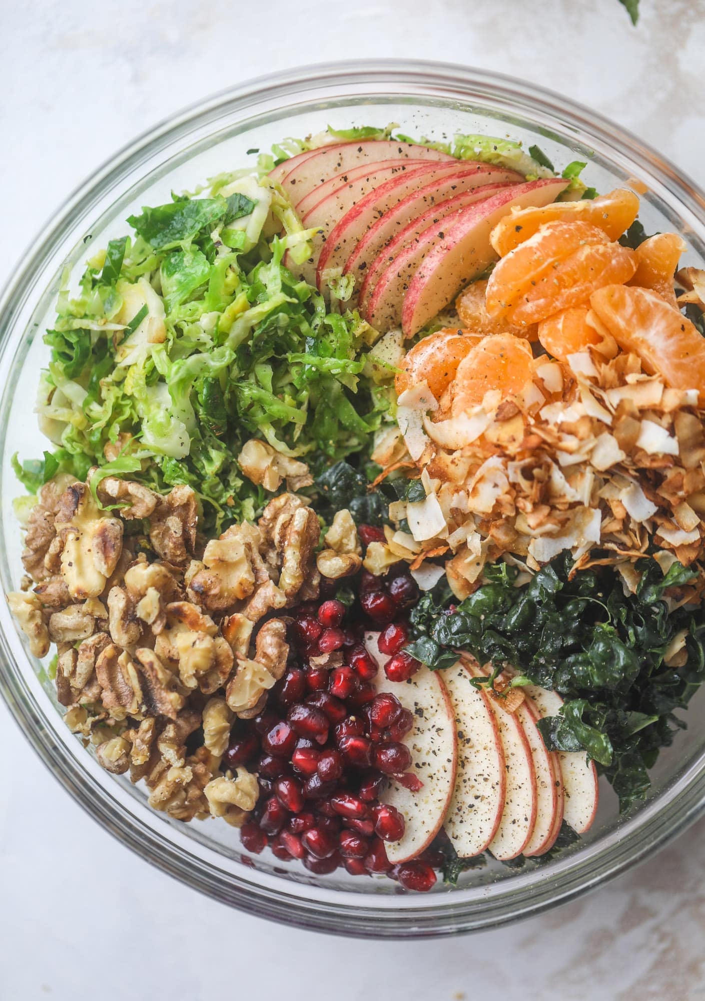 This winter crunch salad is loaded with tons of delicious, crunchy seasonal ingredients. A base of brussels sprouts and kale is topped with sliced apples, satsuma wedges, pomegranate arils, toasted walnuts and savory flaked coconut crunch. Delish! I howsweeteats.com #winter #salad