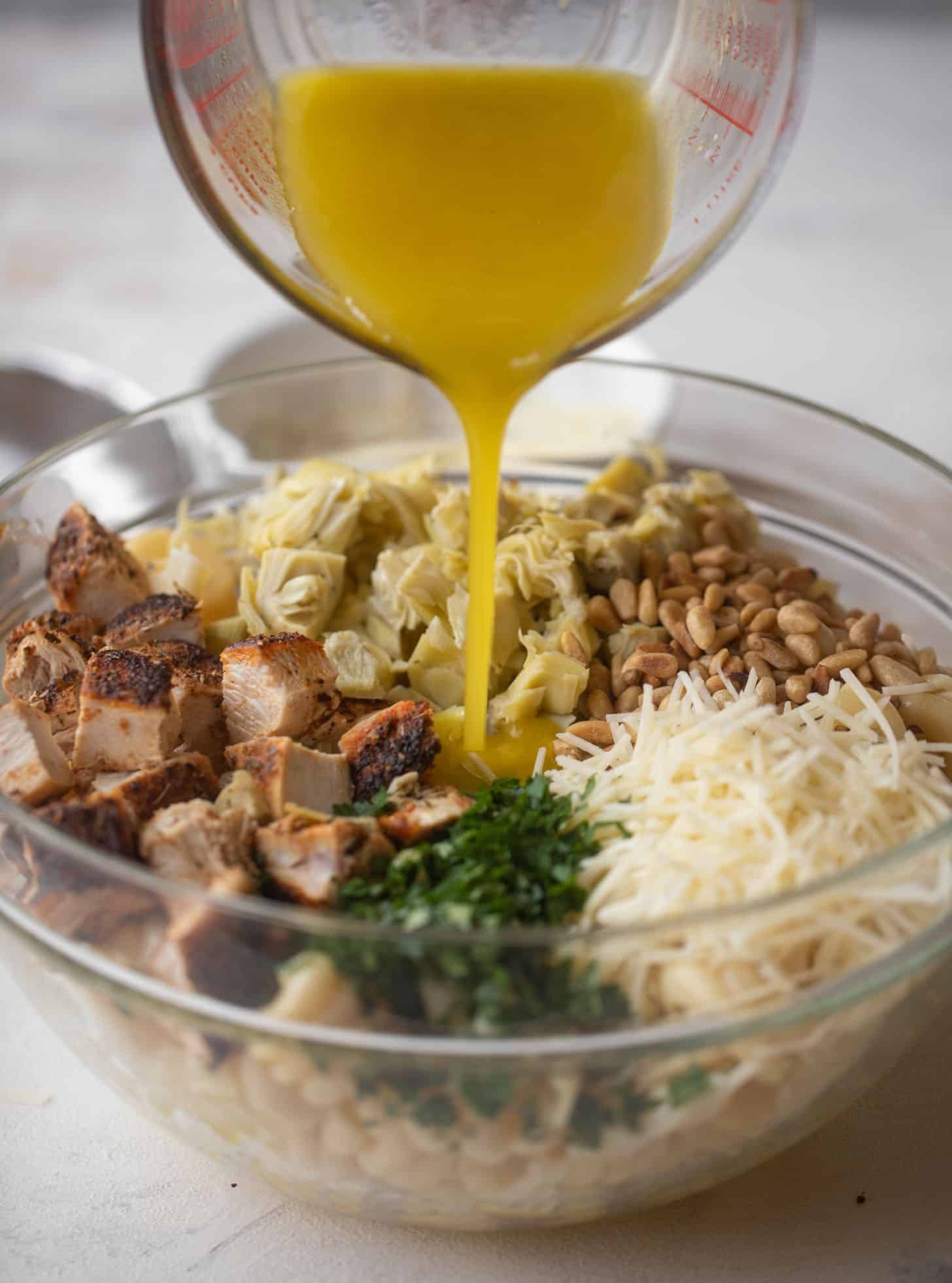 pouring dressing on lemon chicken artichoke pasta salad